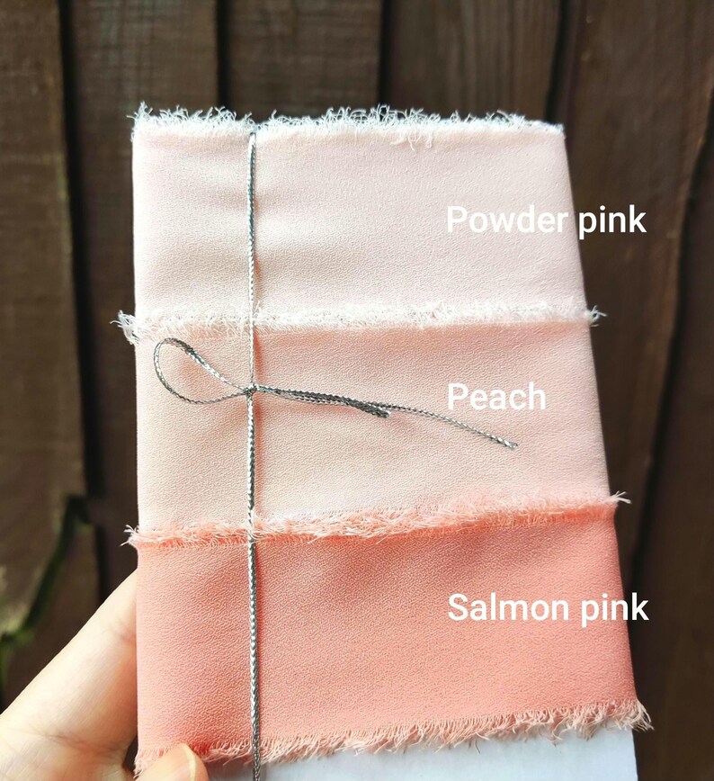 Puede incluir: Tres cintas de tela apiladas con bordes deshilachados, atadas con un fino cord&oacute;n met&aacute;lico plateado. Las cintas est&aacute;n etiquetadas como Powder pink, Peach y Salmon pink, mostrando un degradado de texturas de tela en tonos rosa y naranja.