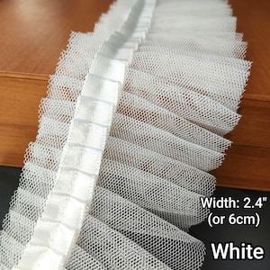 May include: White ruffled lace trim, 2.4 inches (6 cm) wide, with a net-like texture and a satin ribbon detail. The trim is white and suitable for various craft projects.