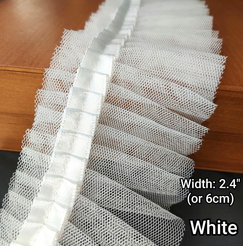May include: White ruffled lace trim, 2.4 inches (6 cm) wide, with a net-like texture and a satin ribbon detail. The trim is white and suitable for various craft projects.