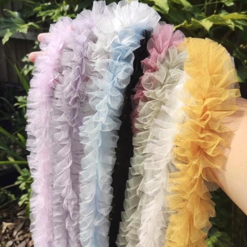 Pu&ograve; includere: Una collezione di strisce di passamaneria in tulle arricciato in una variet&agrave; di colori pastello e vivaci, tra cui viola chiaro, bianco, azzurro, nero, rosa antico, crema e giallo oro, con una trama a rete fine e bordi arricciati.