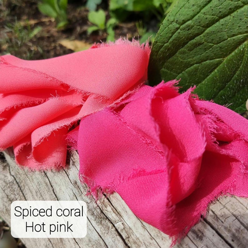 Puede incluir: Dos tiras de cinta de tela deshilachada en colores coral especiado y rosa intenso. Las cintas tienen una apariencia tejida y texturizada con bordes crudos e irregulares. Se ve una etiqueta rectangular blanca con el texto Spiced coral Hot pink.