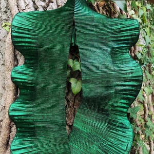 Könnte beinhalten: Dunkelgrüner, plissierter Stoff mit strukturiertem, geripptem Aussehen. Der Stoff ist in eine einzigartige, fließende Form geschnitten. Der Text "Dark green" wird in weißer Schrift in der oberen rechten Ecke angezeigt. Der Stoff wird vor einem Baumstamm präsentiert.