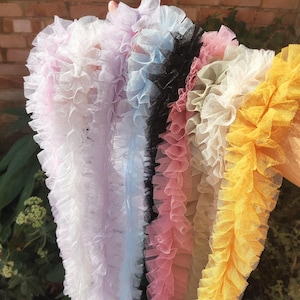 Pu&ograve; includere: Una collezione di strisce di passamaneria in tulle arricciato in vari colori, tra cui viola chiaro, azzurro, nero, rosa antico, beige e giallo brillante. Ogni striscia presenta una consistenza plissettata in tessuto a rete semitrasparente.