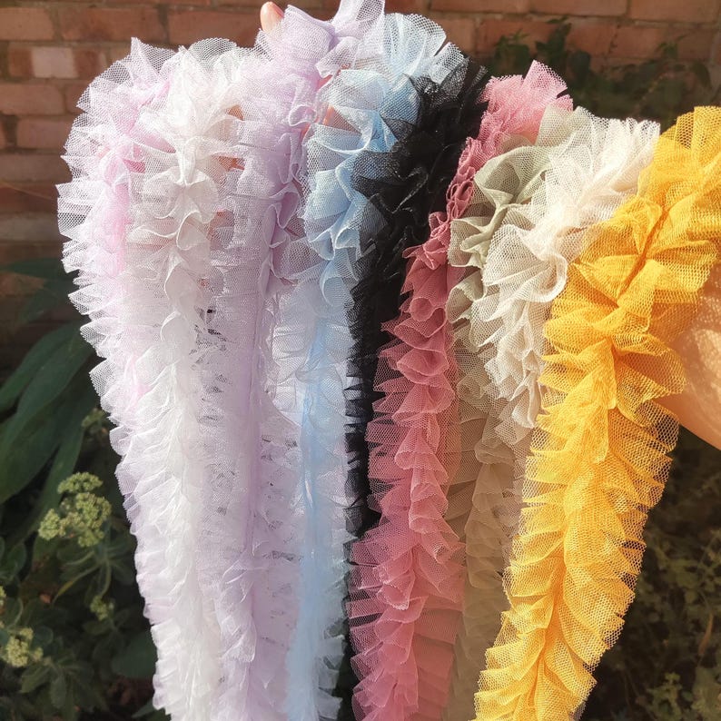 Pu&ograve; includere: Una collezione di strisce di passamaneria in tulle arricciato in vari colori, tra cui viola chiaro, azzurro, nero, rosa antico, beige e giallo brillante. Ogni striscia presenta una consistenza plissettata in tessuto a rete semitrasparente.