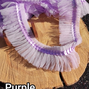 May include: A length of ruffled purple tulle ribbon with a satin ribbon trim. The tulle is a light lavender color, and the satin ribbon is a slightly darker shade of purple. The word "Purple" is printed in white at the bottom of the image.