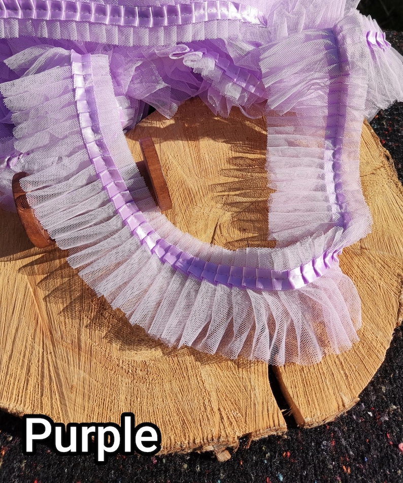 May include: A length of ruffled purple tulle ribbon with a satin ribbon trim. The tulle is a light lavender color, and the satin ribbon is a slightly darker shade of purple. The word "Purple" is printed in white at the bottom of the image.