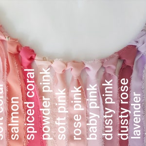 Puede incluir: Una guirnalda decorativa que presenta una serie de tiras de tela deshilachadas atadas a un cord&oacute;n. Los colores est&aacute;n etiquetados como peach, soft coral, salmon, spiced coral, powder pink, soft pink, rose pink, baby pink, dusty pink, dusty rose, lavender, dusty mauve y lilac.