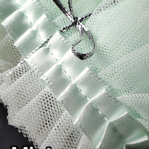 May include: Close-up of a mint green fabric with a delicate, net-like texture. The fabric is accented with satin ribbons and a silver-colored cord, tied in a bow. The word "Mint" is printed in white at the bottom.