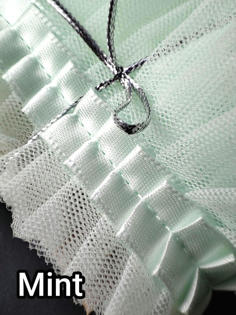 May include: Close-up of a mint green fabric with a delicate, net-like texture. The fabric is accented with satin ribbons and a silver-colored cord, tied in a bow. The word "Mint" is printed in white at the bottom.