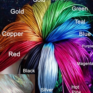 Könnte beinhalten: Eine Sammlung von 1,5 mm breiten Satinschnüren in verschiedenen Farben, darunter Blassgold, Apfelgrün, Grün, Blaugrün, Blau, Lila, Magenta, Pink, Silber, Weiß, Schwarz, Rot, Kupfer und Gold, fächerförmig angeordnet mit entsprechenden Beschriftungen.
