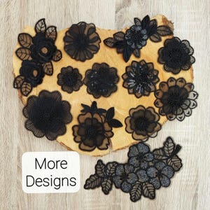 May include: A collection of black floral lace appliques featuring various flower shapes, some with intricate embroidery, sequins, and mesh detailing. A white rectangular label with the black text More Designs is positioned in the lower left corner.