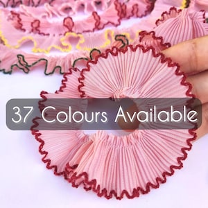 Peut inclure: Un ruban en tissu plissé rose clair avec un bord festonné doté d'une bordure cousue rouge foncé. Le ruban est disposé en motifs circulaires et linéaires. Le texte 37 Colours Available est superposé sur l'image en police blanche sans empattement.