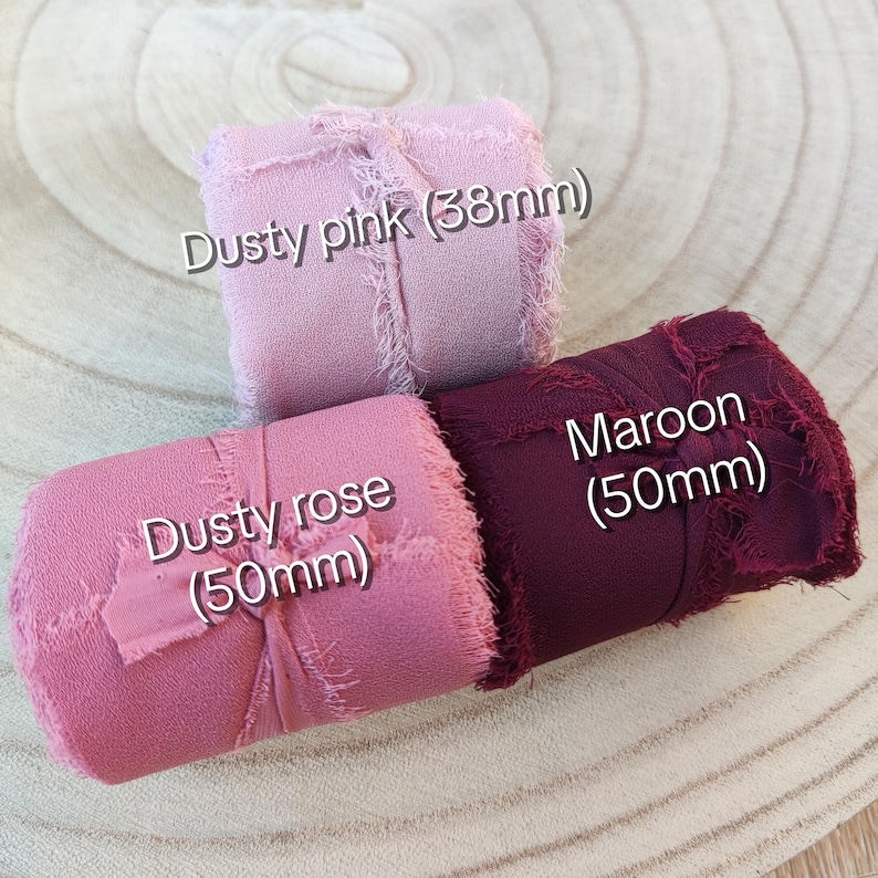 Puede incluir: Tres rollos de cinta con bordes deshilachados en rosa polvoriento, rosa viejo y granate. La cinta rosa polvoriento mide 38 mm de ancho, mientras que las cintas rosa viejo y granate miden 50 mm de ancho cada una. Cada rollo lleva un lazo fino.