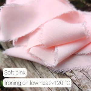 Puede incluir: Una pieza de tela de color rosa suave con bordes crudos y deshilachados. El material tiene una superficie texturizada y est&aacute; drapeado en pliegues sueltos. El texto impreso en la imagen dice: Soft pink, Ironing on low heat~120 &deg;C.
