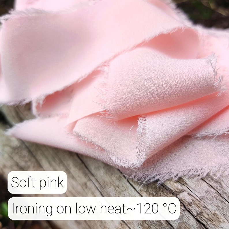 Puede incluir: Una pieza de tela de color rosa suave con bordes crudos y deshilachados. El material tiene una superficie texturizada y est&aacute; drapeado en pliegues sueltos. El texto impreso en la imagen dice: Soft pink, Ironing on low heat~120 &deg;C.