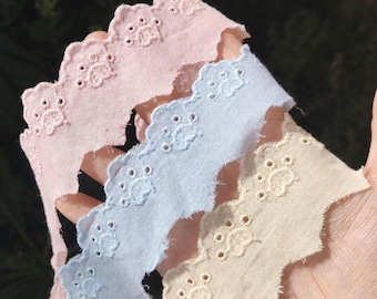 May include: Three strips of scalloped eyelet lace trim in pastel pink, light blue, and cream. Each strip features a repeating embroidered pattern of small paw prints along the scalloped edge, with delicate circular cutouts and stitching.