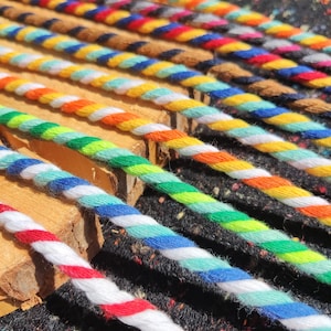 May include: A close-up shot of multiple twisted cords in various colours. The cords, arranged diagonally, display a range of hues such as red and white, blue and white, green and yellow, and orange and white. They are placed on small wooden blocks.