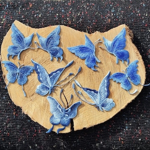 May include: A collection of blue denim butterfly appliques on a wooden surface. The butterflies are various sizes and have a distressed look.