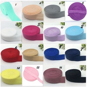 Könnte beinhalten: Sortiment von 16 Farben elastischem Stoffbesatz, jede Farbe ist aufgerollt und mit einer Nummer gekennzeichnet. Die Farben umfassen: hellblau, beige, grau, lila, weiß, rosa, lavendel, hellblau, rot, braun, blau, marineblau, gelb, rosa, kastanienbraun und dunkelblau.