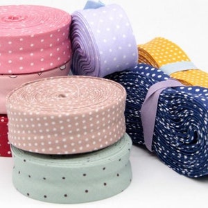 Può includere: Una collezione di rotoli di nastro di tessuto colorato. I rotoli sono in vari colori, tra cui rosa, viola, blu, giallo e verde, con pois e motivi a cuore. Ideale per progetti di artigianato e cucito.