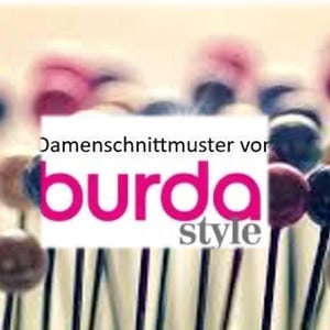 Peut inclure: Gros plan sur une pancarte blanche avec le texte "Damenschnittmuster von burda style" en lettres roses. La pancarte est devant un fond d'épingles à coudre colorées.