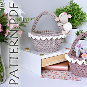 Może przedstawiać: Dwa koszyki na szydełku z białą koronkową lamówką. Jeden kosz jest beżowy i zawiera szydełkowanego baranka. Drugi kosz jest różowy i zawiera szydełkowanego króliczka trzymającego kwiat. Koszyki znajdują się na białym tle z kwiatowym wzorem.