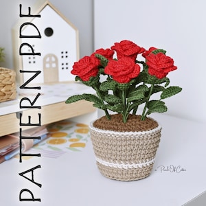 May include: A crocheted flower pot with red roses. The pot is beige with a white stripe and contains brown 'soil'. The roses have green leaves and stems. The text "PATTERN PDF" is on the left side of the image.