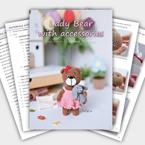 May include: A crochet pattern book titled "Lady Bear with accessories" featuring a crocheted bear wearing a pink dress and holding a gray bunny. The book includes instructions and tips, with additional pages visible.