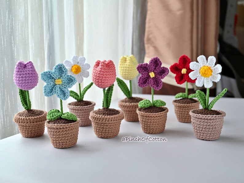 May include: A collection of eight crocheted flower arrangements in small brown pots. The flowers are a variety of colors, including purple, pink, blue, yellow, white, and red.