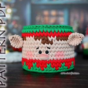 May include: Crocheted elf-themed basket with green, red, brown, and white yarn. The basket has a face with black eyes and a pink nose. The text "aPinchOfCotton" is visible at the bottom of the image.