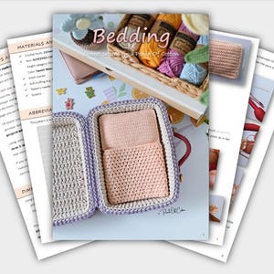 May include: A crochet pattern book titled "Bedding" with a light pink crochet case containing two crochet items. The book features a basket of yarn and a crochet flower. Several pages of instructions are visible.