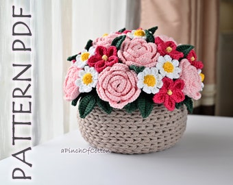 May include: A crocheted flower bouquet in a brown basket. The bouquet includes pink roses, white daisies, and red flowers. The text "aPinchOfCotton" is visible below the basket.