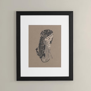 Puede incluir: Lámina artística enmarcada en negro con una ilustración detallada en blanco y negro de una criatura parecida a un reptil. La obra de arte está sobre un fondo beige con un passe-partout blanco. La impresión está colgada en una pared de color neutro.
