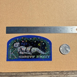 May include: A blue sticker with a sleeping knight in silver armor, the text "NIGHTY NIGHT", and a crescent moon. The sticker is approximately 4 inches long.