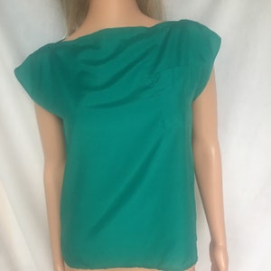 May include: A teal green short-sleeved blouse with a scoop neck and a small pocket on the left side.