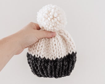 May include: A white and black knitted beanie with a white pom pom on top.