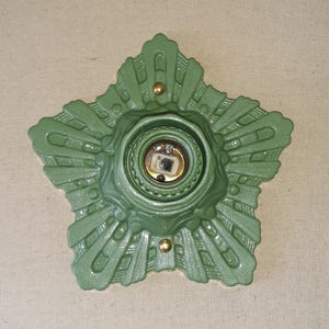 May include: A green metal star-shaped ceiling fixture with a decorative design. The fixture has a central opening for a light bulb.