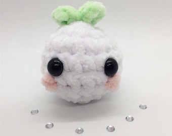 May include: A handmade white crochet plushie with large black eyes and light pink cheeks. The plushie has two small green tufts on top. Several small, clear rhinestones are scattered around the plushie.
