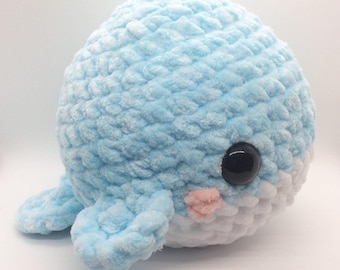 May include: A crocheted blue and white whale plush toy with black eyes and a pink mouth. The whale is made with a soft, fuzzy yarn.