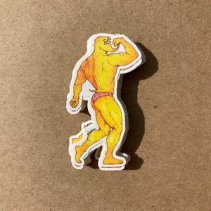 May include: A yellow sticker of a cartoon character flexing their muscles. The character is wearing a pink and white patterned swimsuit. The sticker is on a brown background.