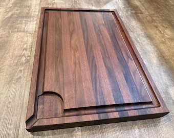 Op de afbeelding: Een rechthoekige houten snijplank met een donkerbruine afwerking. De plank heeft een sapgroef rondom en een afgeronde uitsparing in een hoek. De houtnerf is zichtbaar. Dit keukenartikel is ideaal voor het bereiden van voedsel. Afmetingen zijn ongeveer 40 cm x 30 cm.