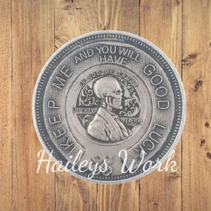 May include: A circular silver-toned metal coin featuring a skeleton profile in the center, with the text "IN GOD WE TRUST", "LIBERTY", and "1959". The outer rim displays the engraved text "KEEP ME AND YOU WILL HAVE GOOD LUCK".