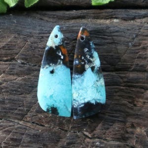 May include: A pair of teardrop-shaped turquoise cabochons with black and brown marbling. The stones have a drilled hole at the top for jewelry making.