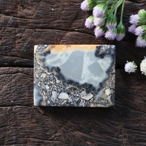 May include: A grey and black agate stone with a white and orange pattern. The stone is rectangular and has a smooth surface.