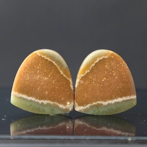 Könnte beinhalten: Zwei tropfenförmige Cabochons aus poliertem grünem und braunem Achat. Die Steine haben eine geschichtete, gebänderte Optik mit einem weißen Rand.