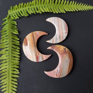 May include: Three agate crescent moon shaped slices in shades of brown, white, and orange. The slices are arranged in a triangular pattern.