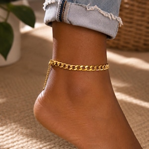 May include: A gold-toned anklet featuring a classic curb chain design. The jewelry piece includes a delicate extender chain with small circular links, providing an adjustable fit around the ankle. The metal has a polished, reflective finish.