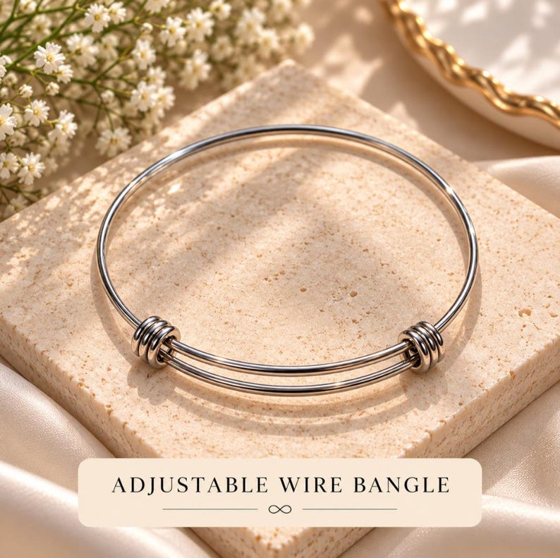 May include: A silver-toned adjustable wire bangle featuring a double-loop design with two sets of three coiled wire accents on each side. The bracelet has a smooth, polished metallic finish and includes the text ADJUSTABLE WIRE BANGLE.