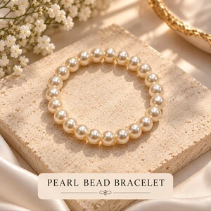 May include: A circular bracelet composed of uniform, cream-colored spherical pearl beads. The bracelet is arranged in a ring shape. A rectangular label at the bottom features the text PEARL BEAD BRACELET in black capital letters.
