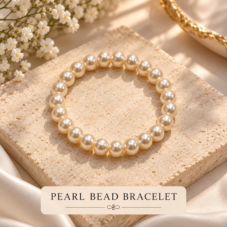 May include: A circular bracelet composed of uniform, cream-colored spherical pearl beads. The bracelet is arranged in a ring shape. A rectangular label at the bottom features the text PEARL BEAD BRACELET in black capital letters.